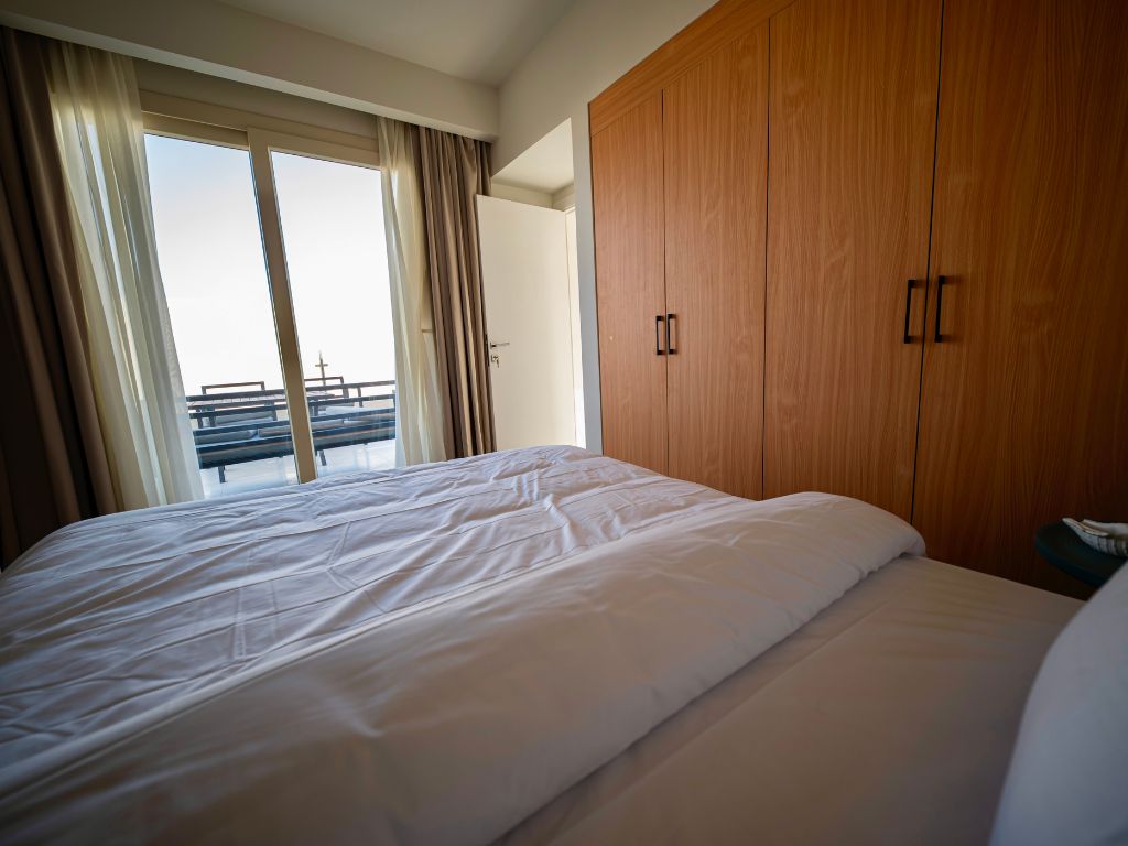 Fitted wooden wardrobes beside a bed and balcony doors in an iL Bayou Laguna furnished interior