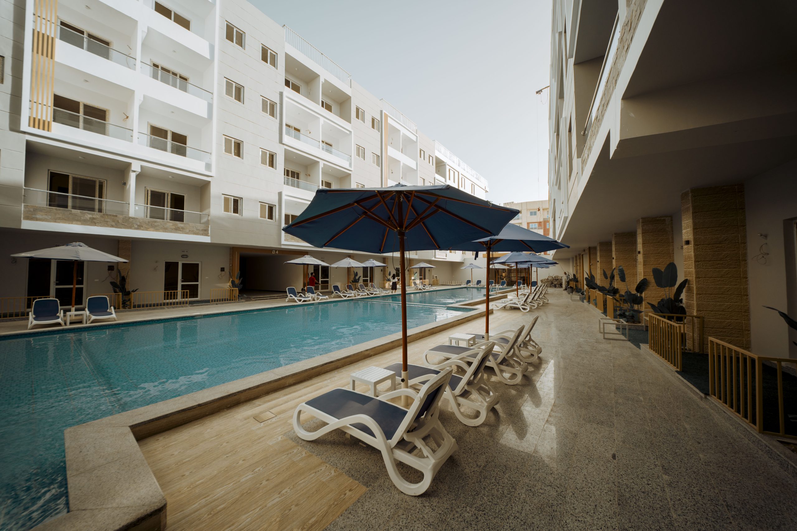 Mark Resort poolside walkway with sun loungers, blue parasols and apartment balconies