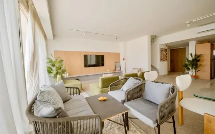 Armchairs and a small table beside tall curtained windows in an iL Bayou Laguna furnished living room